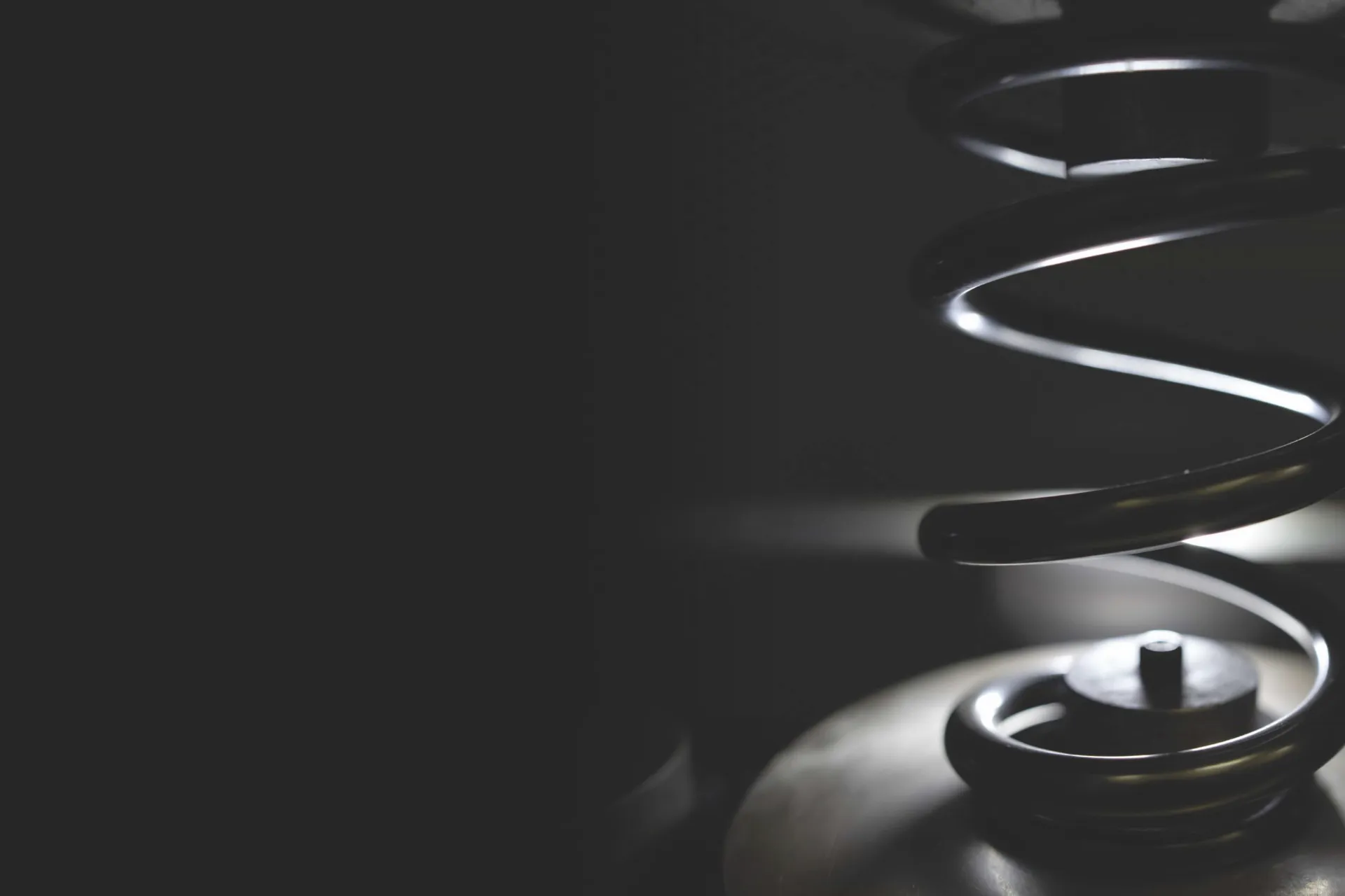 Close-up of a heavy-duty metal compression spring in low light, highlighting its coiled structure and industrial setting.