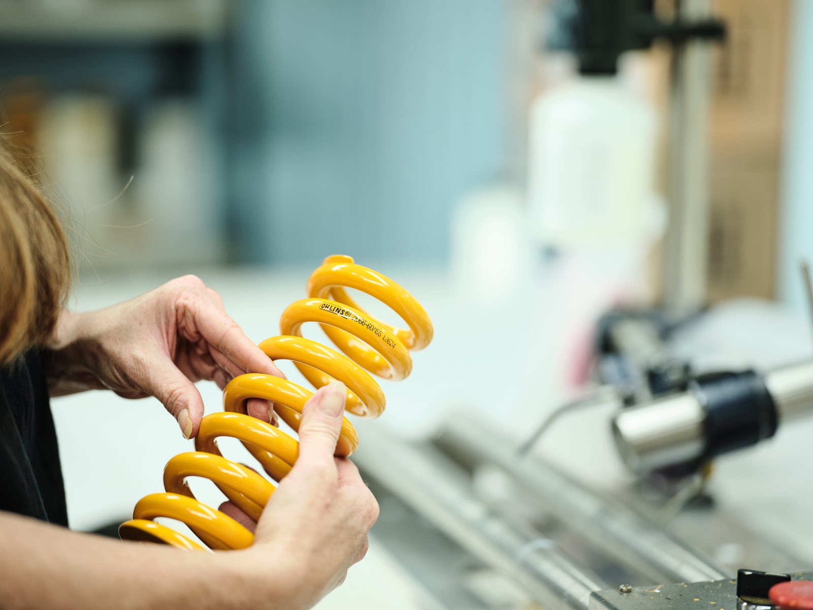 A person holds a yellow, heavy-duty compression spring in a factory.
