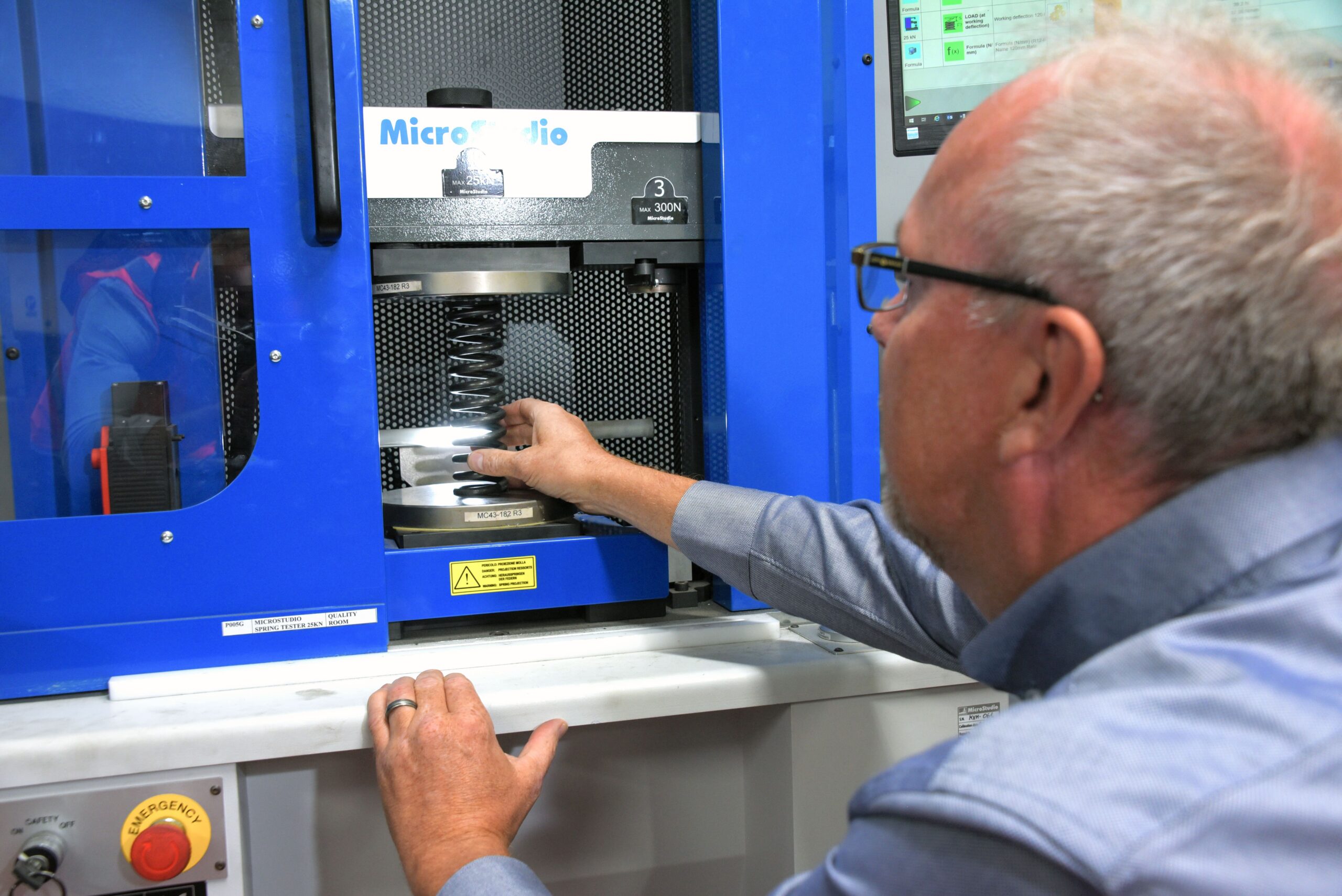 A Lesjöfors employee putting a coil spring in a spring testing machine to perform a coil stress test using high-precision compression equipment.