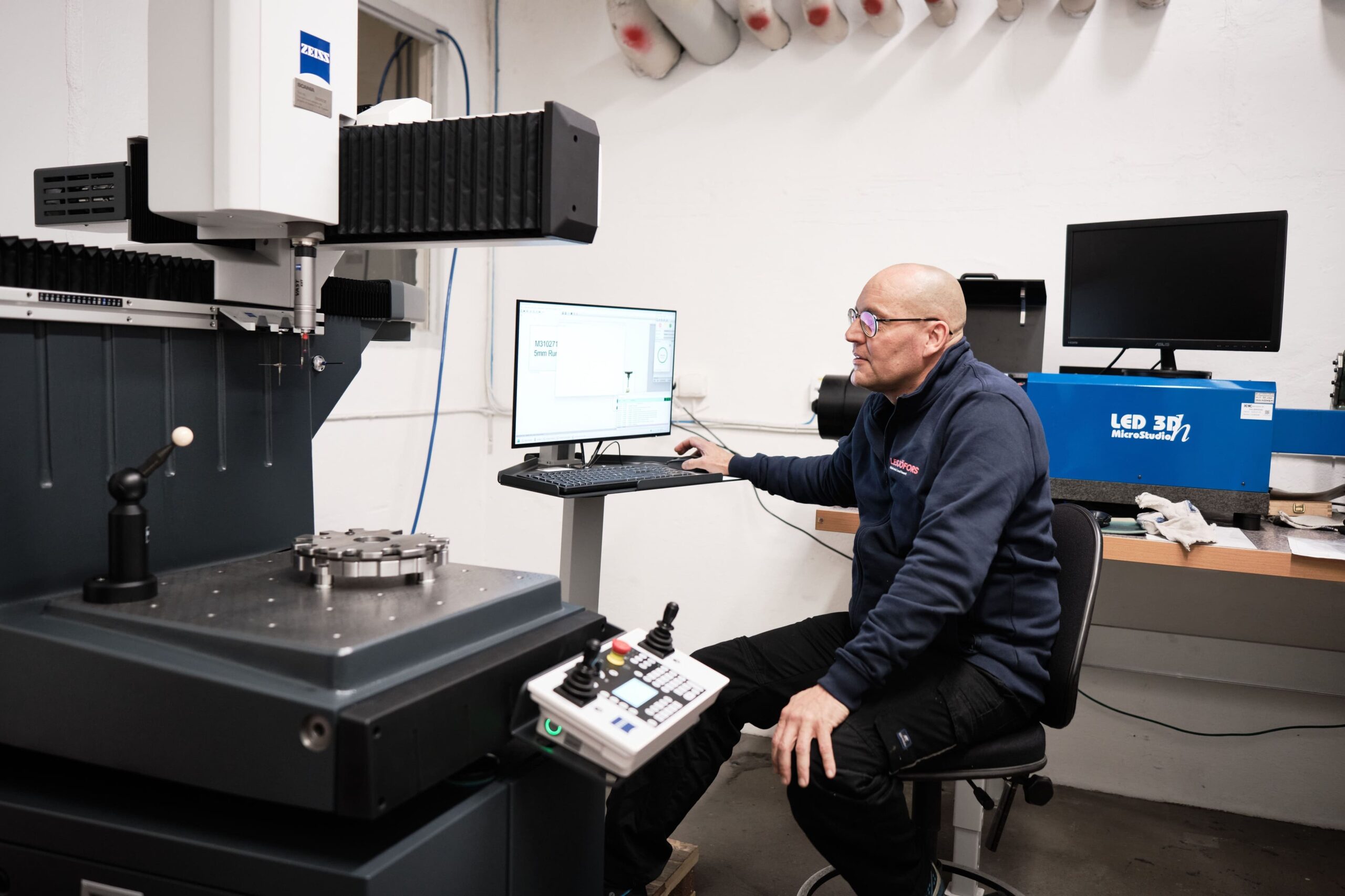 A Lesjöfors employee sitting by a computer and a coil spring testing machine carrying out work to aid spring design.